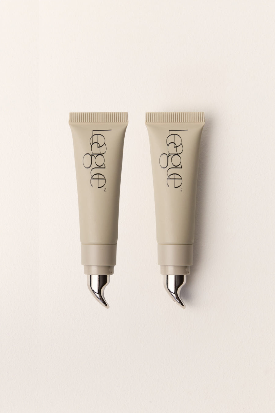 Two beige cosmetic tubes with metal applicators and 'League' branding on a light background