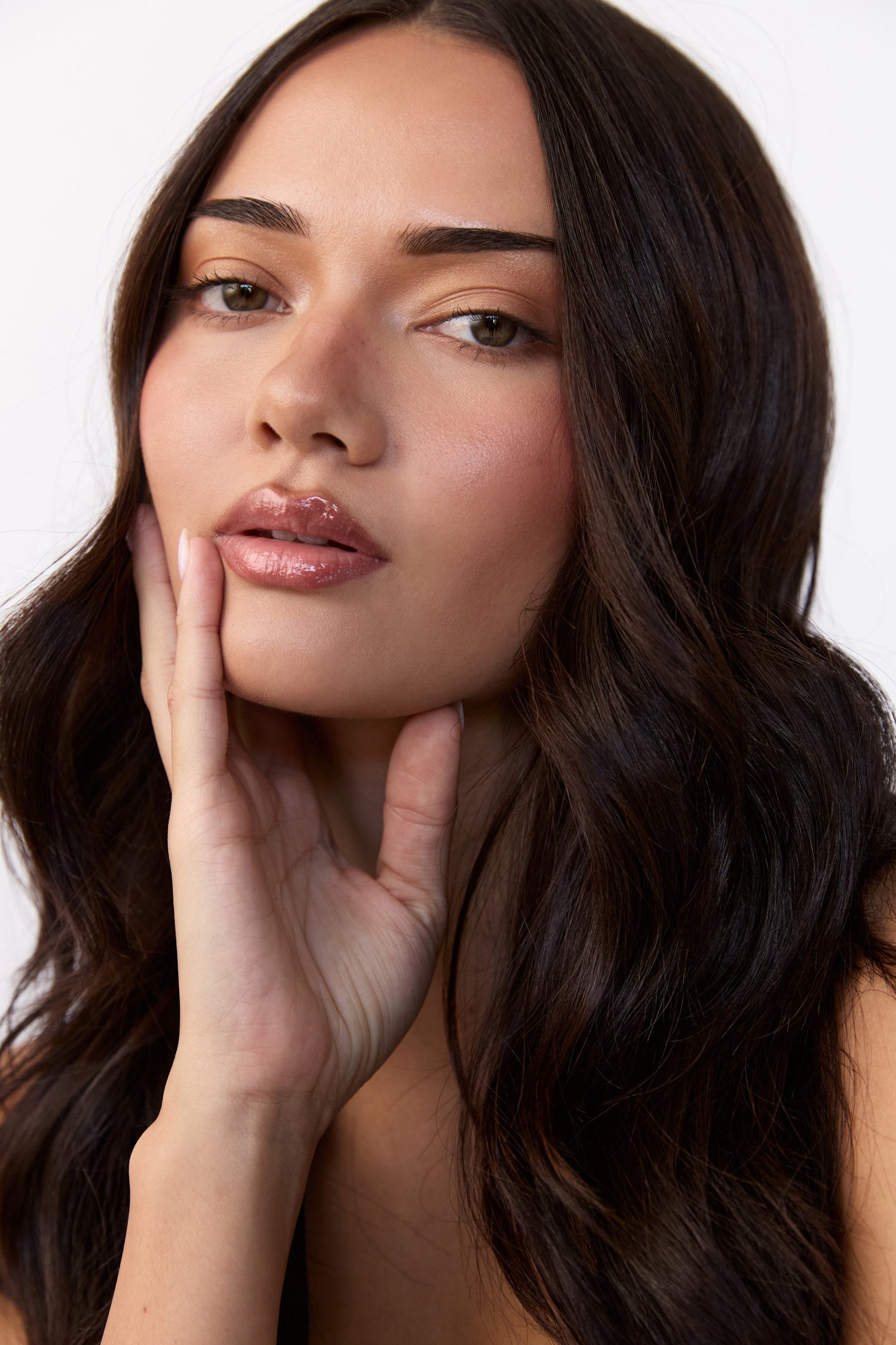 Woman with long dark hair touching her face against a neutral background