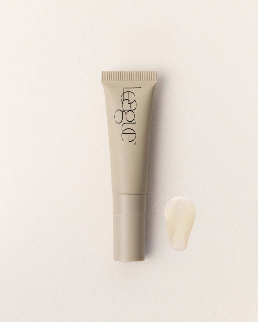 Cosmetic tube with applicator and a clear product swatch on a light beige background