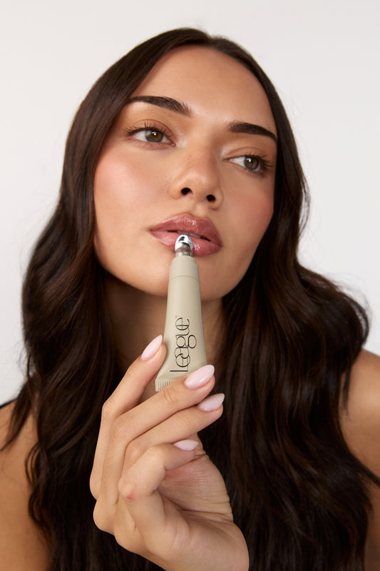Woman holding a lip serum with a visible brand name league against a plain background